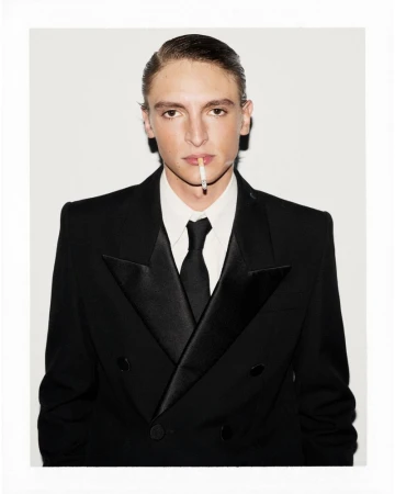 Portrait of a young adult male in a black suit with a cigarette in his mouth against a white background in a photo studio.