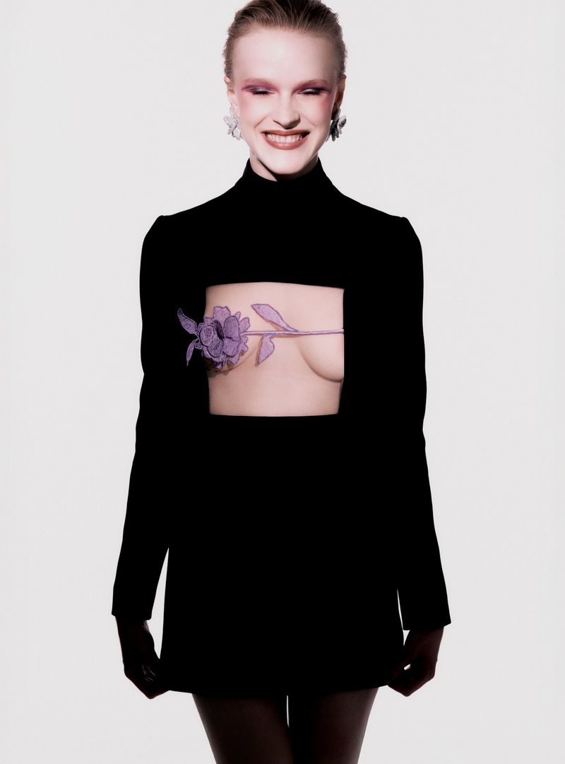 Portrait of a woman with pink eye makeup and wearing a black dress with a flower graphic on her midsection against a white backdrop.
