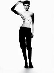 Model wearing a dark cap, halter top, and black trousers against a bright white background in a studio fashion portrait.