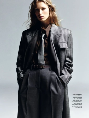 Fashion editorial shot of a woman with long blonde hair wearing a gray suit with a brown shirt and tie in a photo studio.