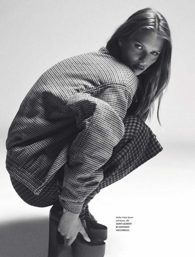 A fashion shot in black and white featuring a young woman in a patterned jacket and matching skirt, posed in a crouch with platform shoes.