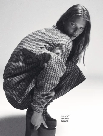 A fashion shot in black and white featuring a young woman in a patterned jacket and matching skirt, posed in a crouch with platform shoes.