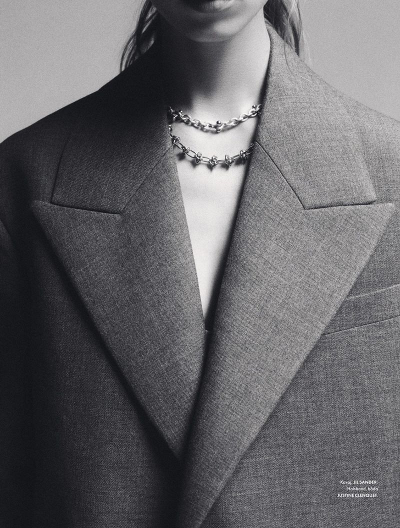 Monochrome portrait of a woman wearing a grey wool blazer, and a layered silver chain necklace with gemstone embellishments.