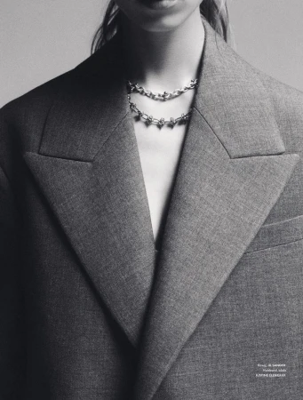 Monochrome portrait of a woman wearing a grey wool blazer, and a layered silver chain necklace with gemstone embellishments.