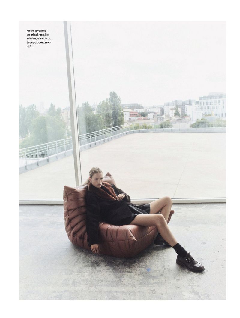 A fashion shot of a woman relaxing on a beanbag chair in an indoor urban setting with large windows overlooking a city.