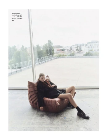 A fashion shot of a woman relaxing on a beanbag chair in an indoor urban setting with large windows overlooking a city.