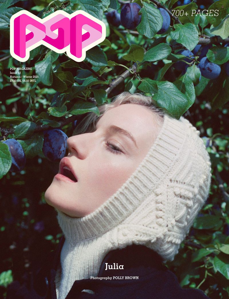 Magazine cover featuring a woman with fair skin wearing a knitted head covering, photographed outdoors among plum tree branches and leaves.