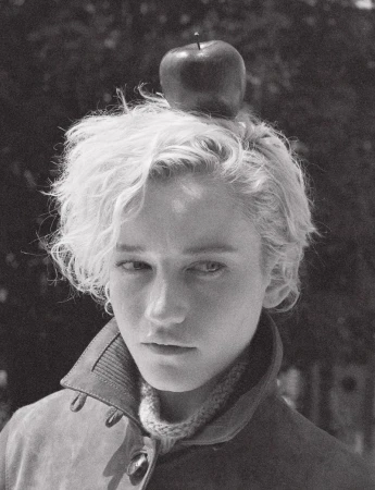 Black and white portrait of Julia Garner balancing an apple on her head, wearing a high-collared jacket for Pop Magazine.