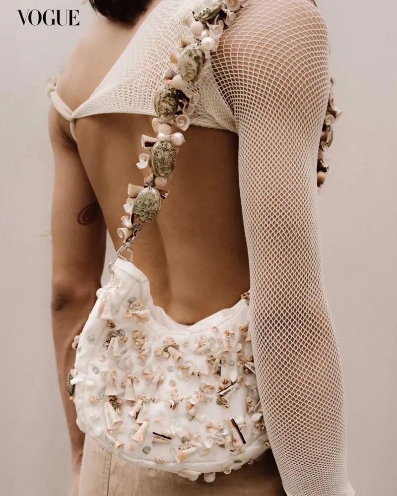 Model wearing a shell-embellished top and carrying a matching handbag, posing in a studio setting for a high fashion shoot.