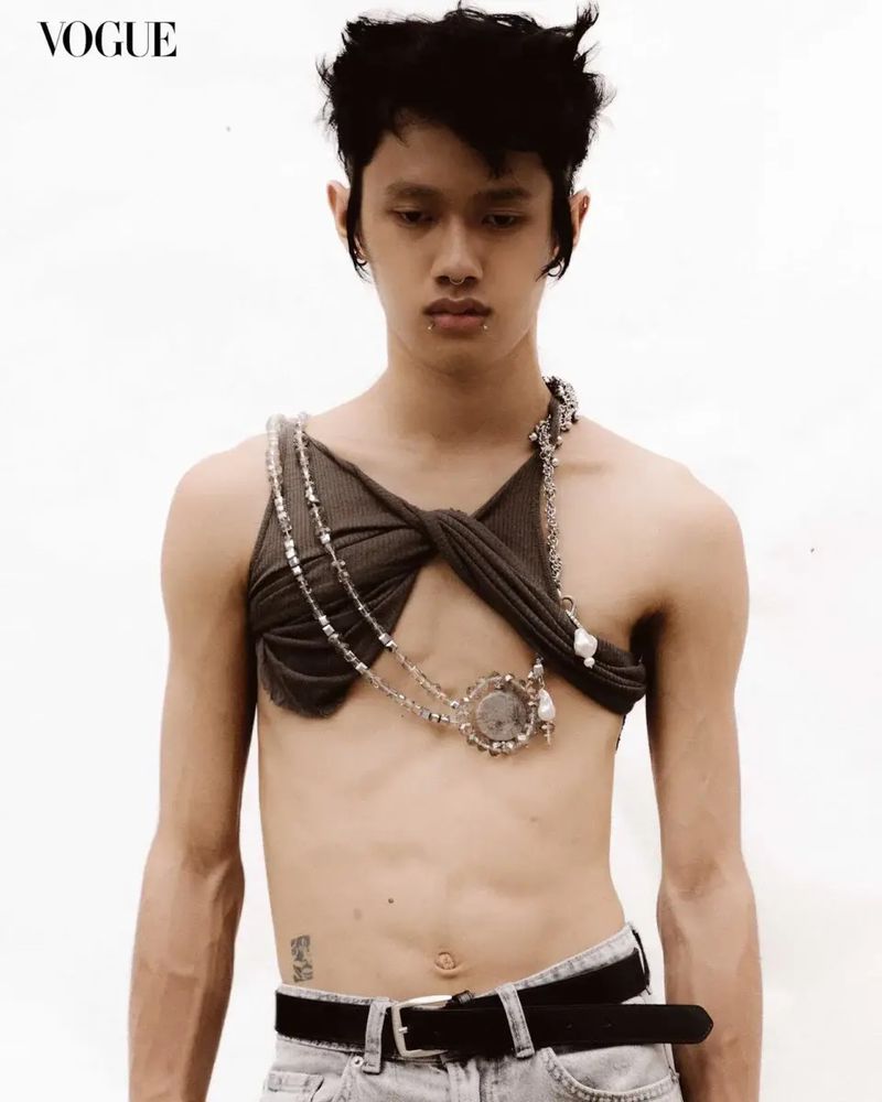 A shirtless person with fair skin poses in a studio setting. The person is wearing light wash jeans and a knotted top.