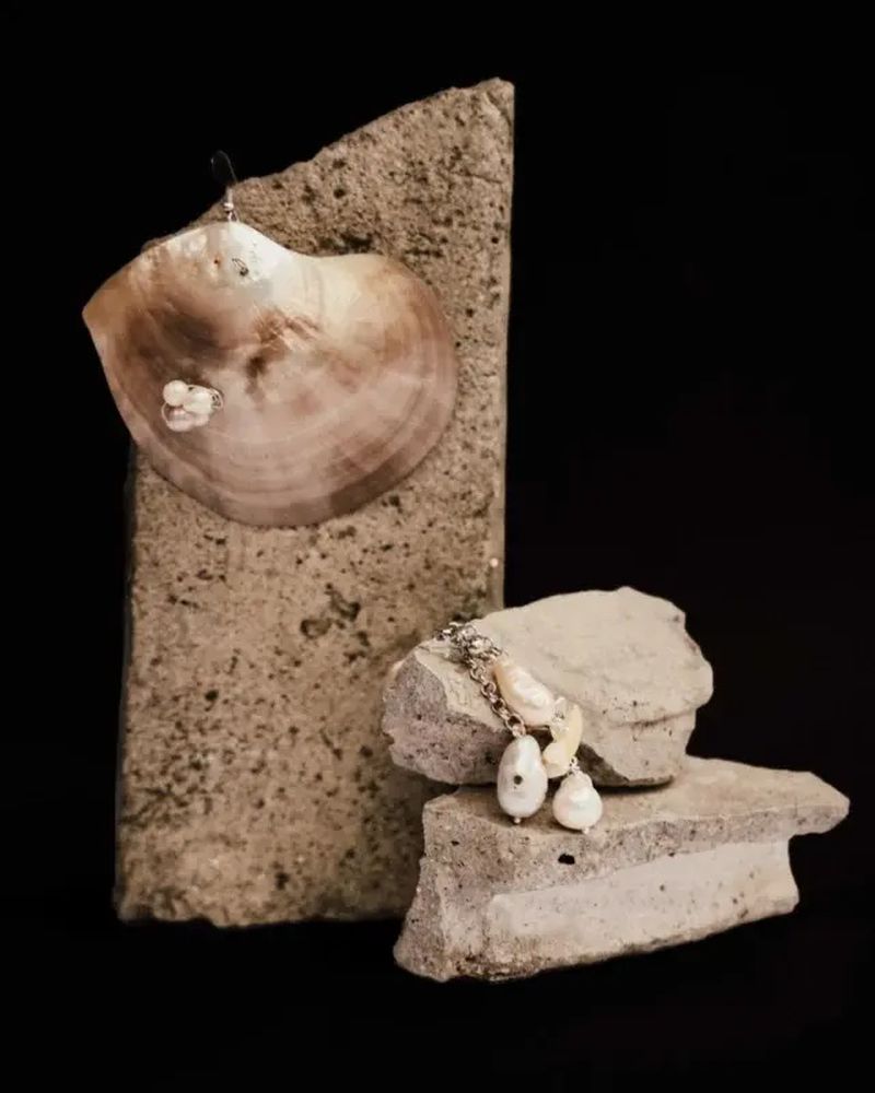 Elegant pearl and shell earrings displayed on textured stone against a dark background, showcasing textures and neutral tones.