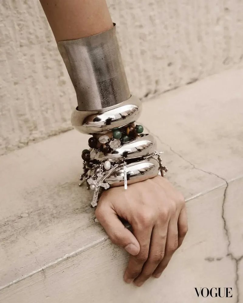 Close-up of a woman's arm adorned with multiple silver bangles and beaded bracelets, set against a neutral textured background.