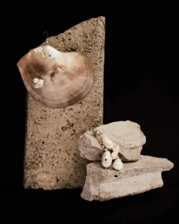 Pearl earrings displayed on a polished seashell and rough stone slabs against a black backdrop.