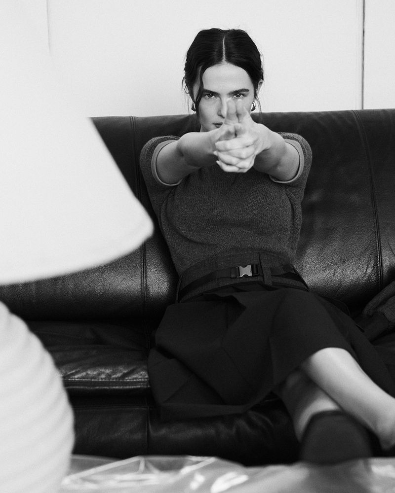 Black and white portrait of woman posing with her hands up like she's holding a gun, sitting on a couch indoors.