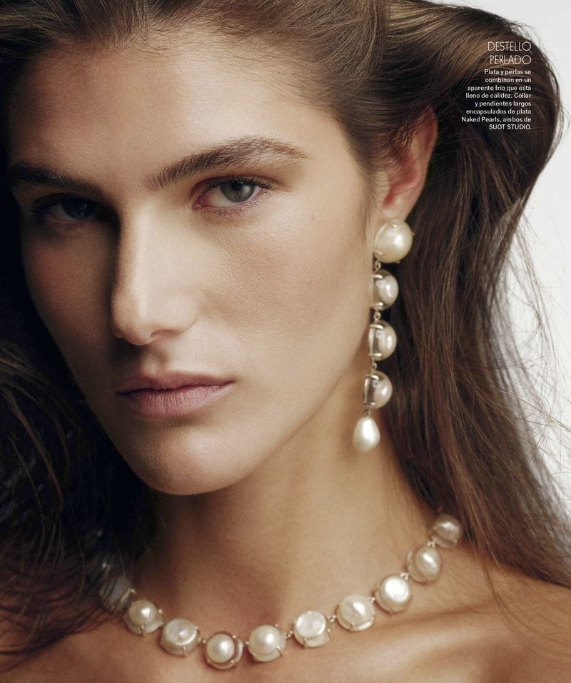 Close-up of a woman with pearl jewelry, showcasing a necklace and dangling earrings in a studio setting, beauty shot, hair styled back.