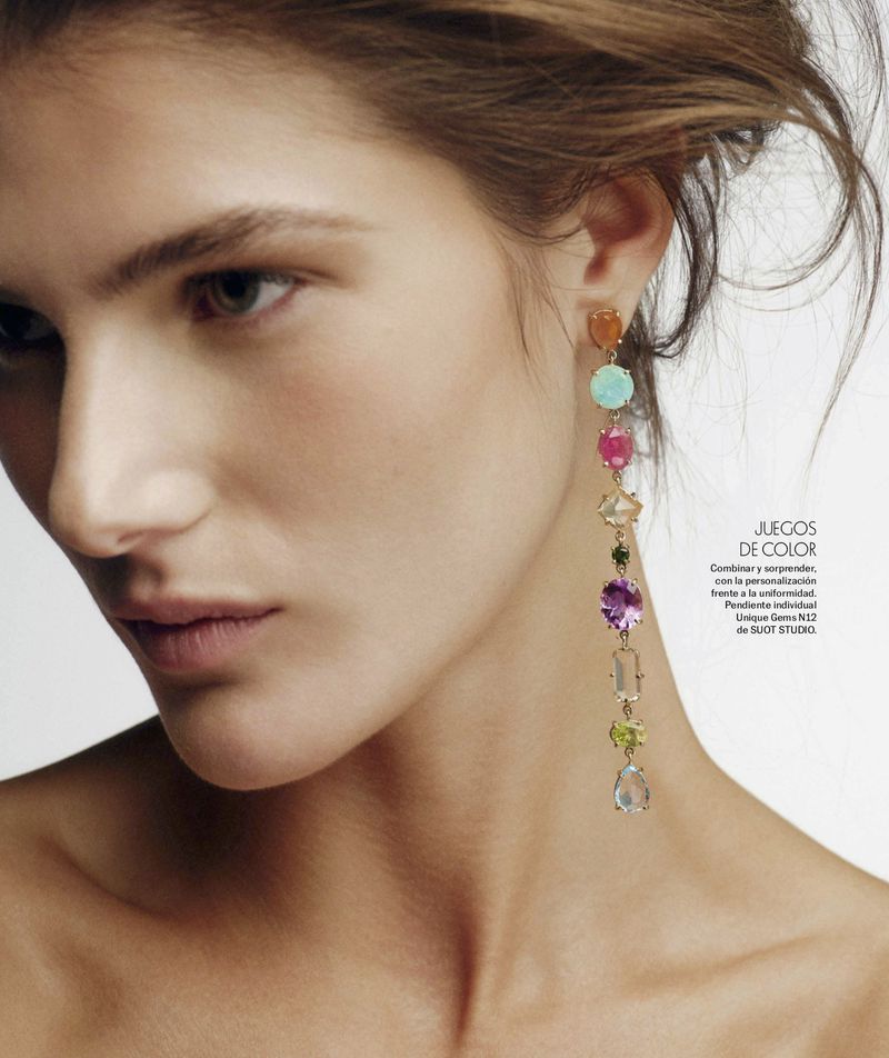 Close-up portrait of a woman wearing long colorful gemstone earrings against a plain white background