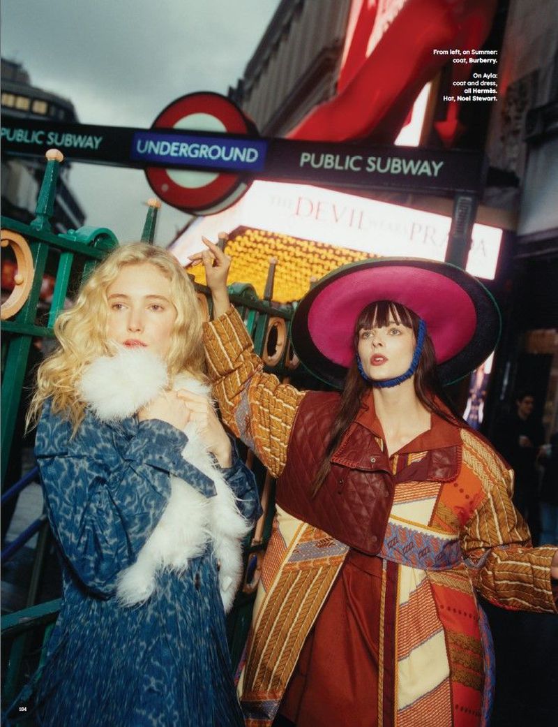 Two fashion models pose in front of the Underground subway sign in London, showcasing unique outerwear and stylish accessories.