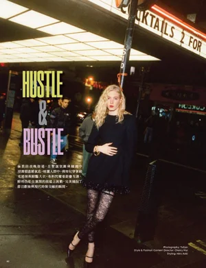 Blonde woman wearing a black dress and patterned tights posing on a wet city street at night under neon signs