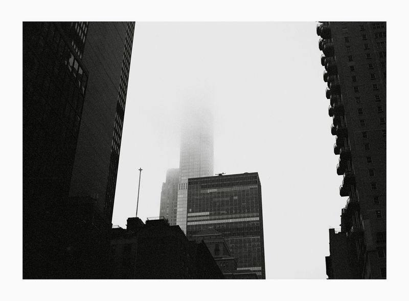Low-angle black and white shot of New York City skyscrapers shrouded in fog, creating a moody urban landscape and architectural scene.