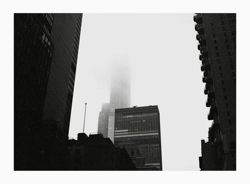 Low-angle black and white shot of New York City skyscrapers shrouded in fog, creating a moody urban landscape and architectural scene.
