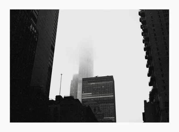 Low-angle black and white shot of New York City skyscrapers shrouded in fog, creating a moody urban landscape and architectural scene.