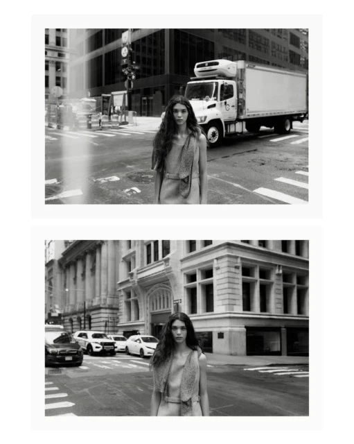 Black and white fashion portrait of a woman with long dark hair wearing a sleeveless dress, standing on a city street with buildings and cars.