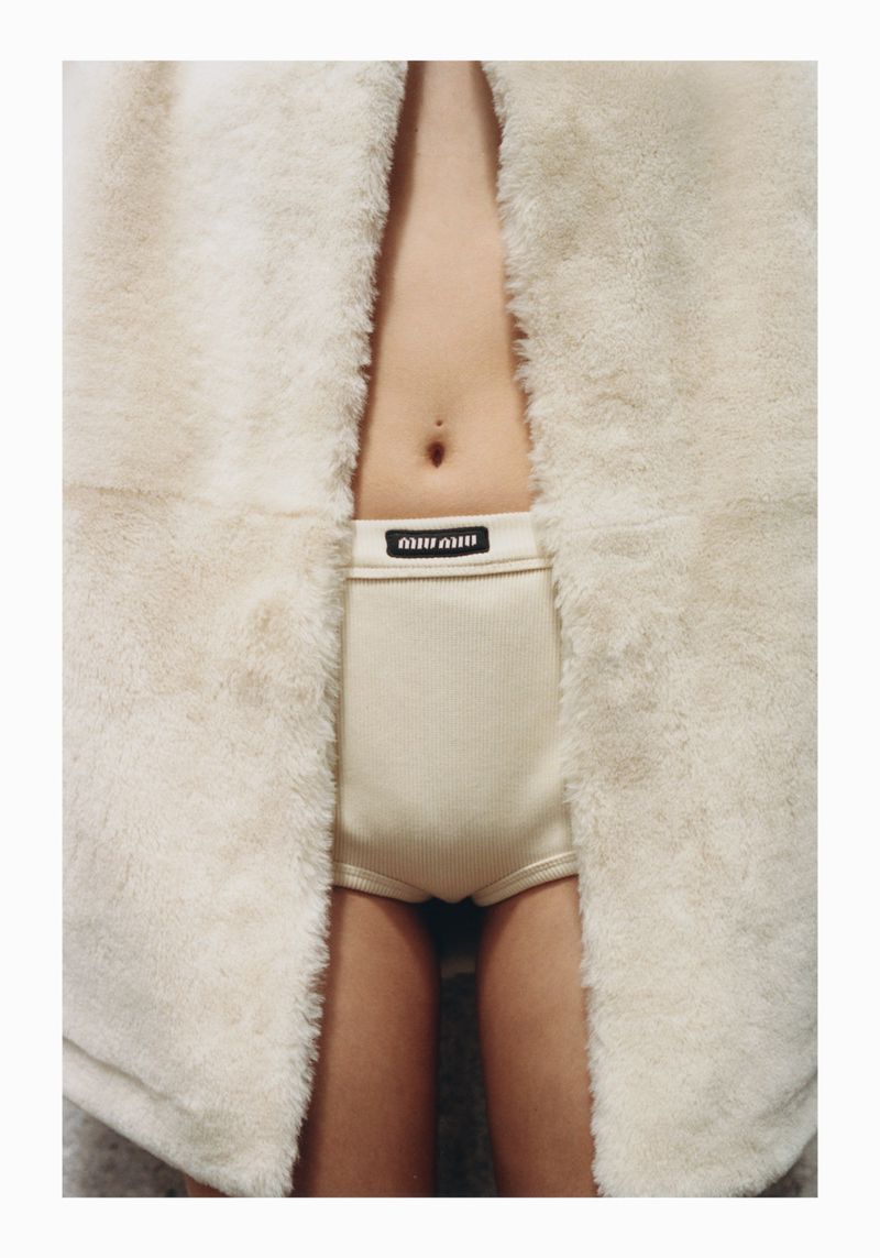 Close-up of a child wearing Miu Miu branded underwear, showcasing the garment's design and fit, partially framed by a fur coat.