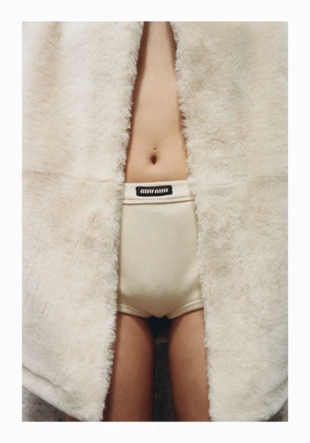 Close-up of a child wearing Miu Miu branded underwear, showcasing the garment's design and fit, partially framed by a fur coat.