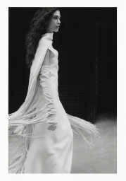 A female model wearing a long white dress with fringe details against a dark background in New York for Vogue Polska.