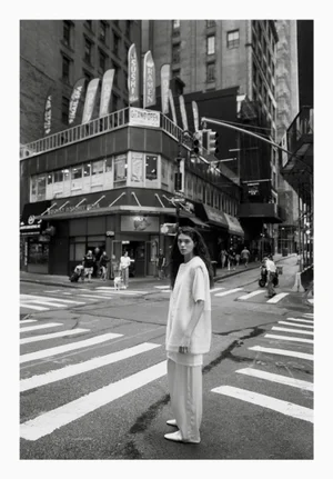 Model Marina Moioli stands in a New York City street crosswalk wearing a light tunic and matching wide trousers in black and white.