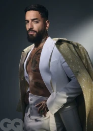 Maluma posing shirtless under an open white suit jacket with a draped gold textured coat for GQ Mexico.
