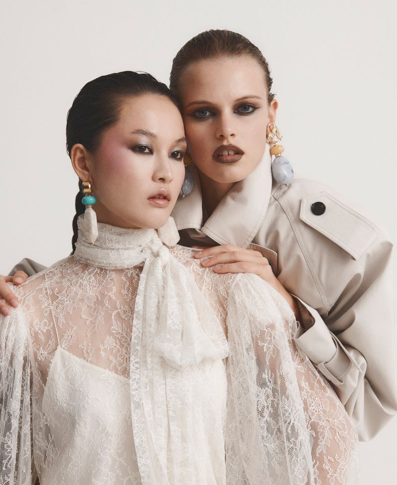 Xin Xie and Nikita Kichaeva posing in a white lace blouse and beige trench coat for Harper's Bazaar Mexico.