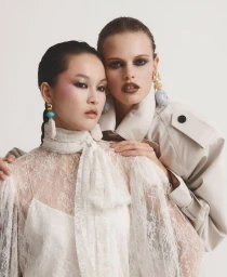 Xin Xie and Nikita Kichaeva posing in a white lace blouse and beige trench coat for Harper's Bazaar Mexico.