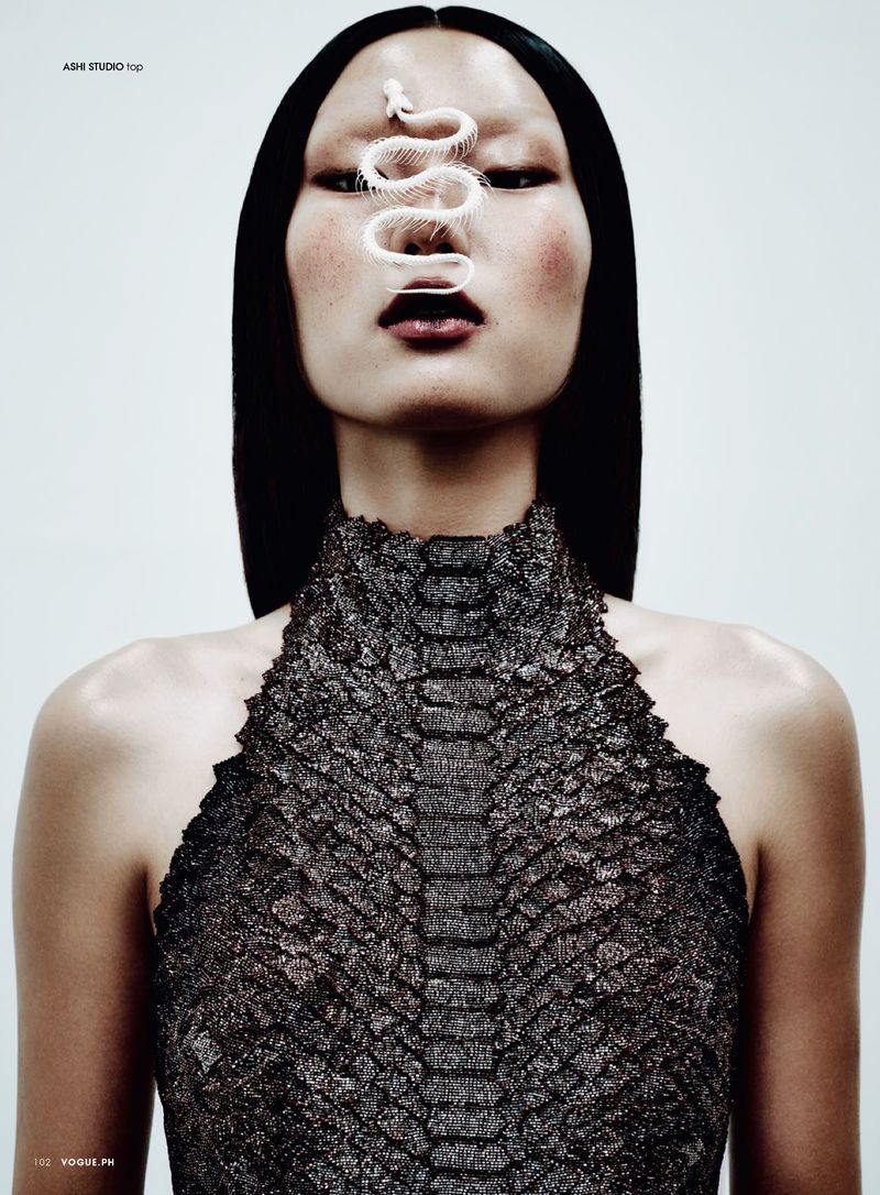 Glamour portrait of an Asian woman with black hair wearing a dress with a snake-like pattern, featuring a decorative snake skeleton.