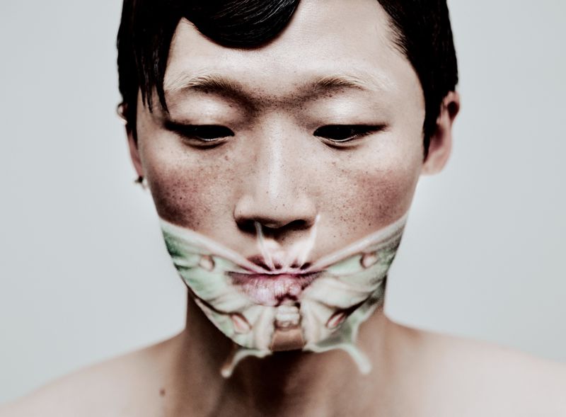 Close-up portrait of an adult with a butterfly graphic overlaying the mouth area, set against a clean, neutral background.