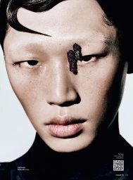Close-up beauty portrait of model Gwonho Oh with textured dark crystal embellishments near the inner eye on a white studio background.