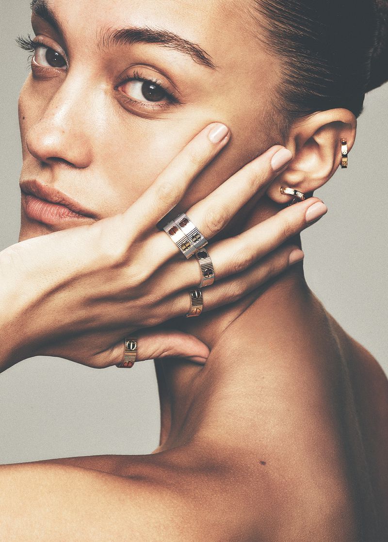 Close-up portrait of model Aida Atarssa posing with a ring-adorned hand against her cheek before a plain studio background.