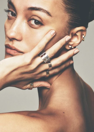 Close-up portrait of model Aida Atarssa posing with a ring-adorned hand against her cheek before a plain studio background.