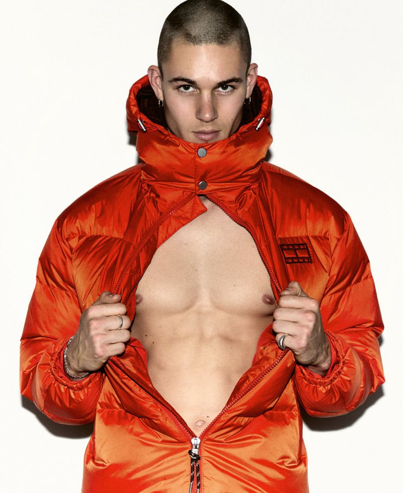Adult man wearing a bright orange puffer jacket and rings in a studio portrait with white background. Looking at the camera.