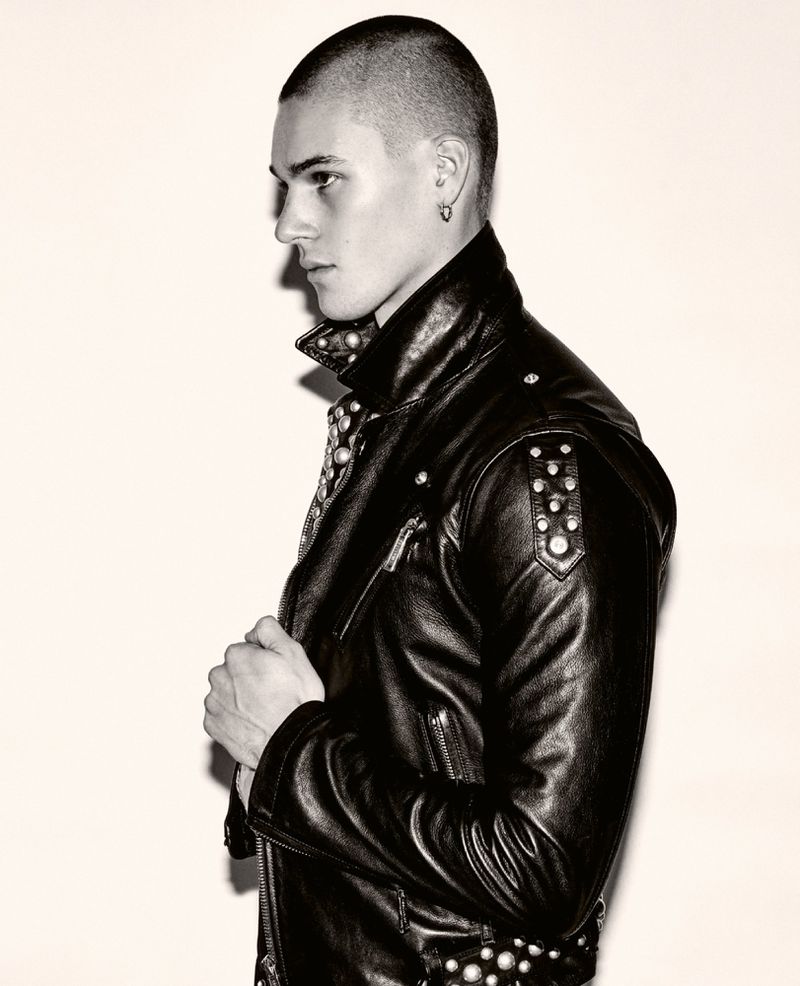 Portrait of adult male with buzzed hair wearing studded leather jacket against plain backdrop in photo studio with directional lighting.
