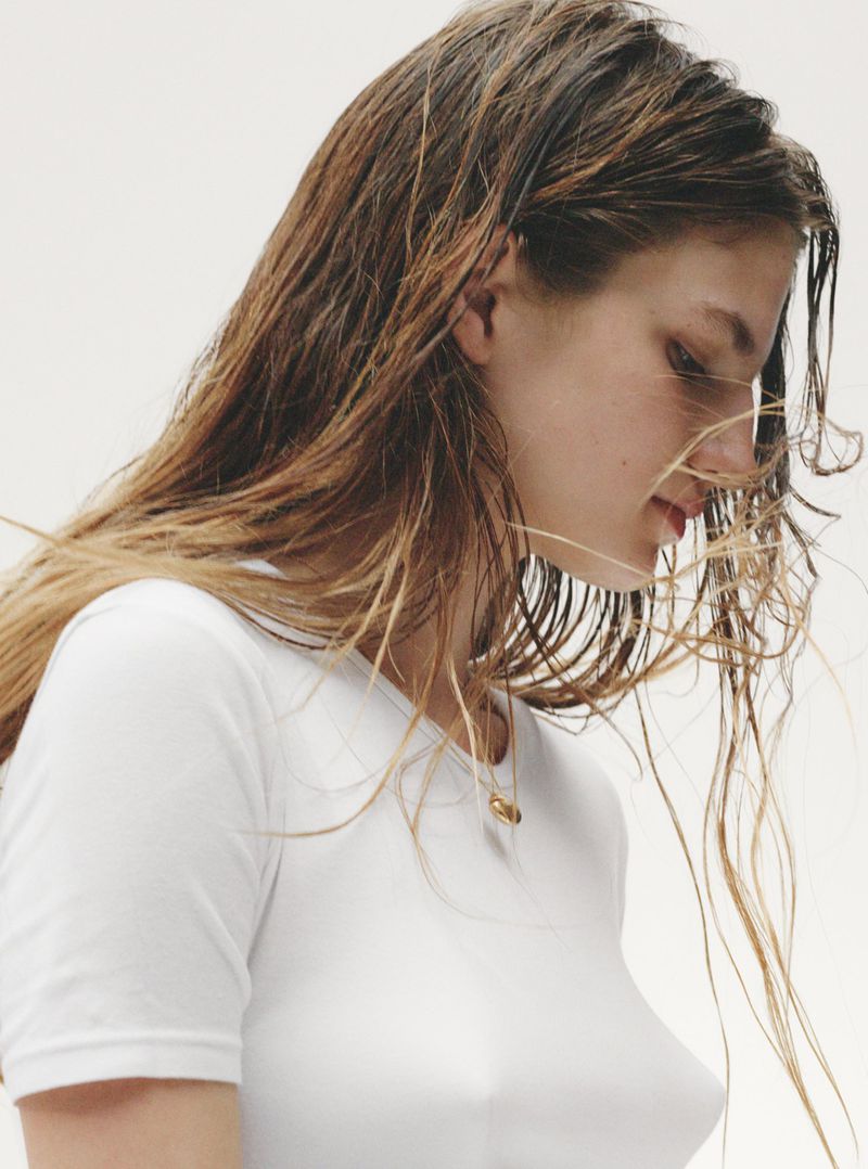 Profile close-up of model Anne Floor Wetemans with damp hair wearing a white t-shirt against a plain white background.