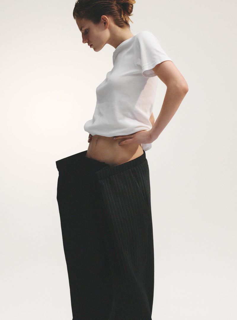 Fashion shot of an adult woman in a white T-shirt and a loose black skirt against a white backdrop in a photo studio.