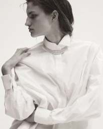 Model Anne Floor Wetemans wearing an oversized white collared shirt and pearl choker necklace against a white backdrop.