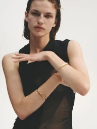 Model Anne Floor Wetemans in a sleeveless black top posing with gold bracelets against a white background.