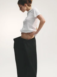 Model Anne Floor Wetemans wearing a white t-shirt and exaggerated oversized black pinstripe trousers against a white backdrop.