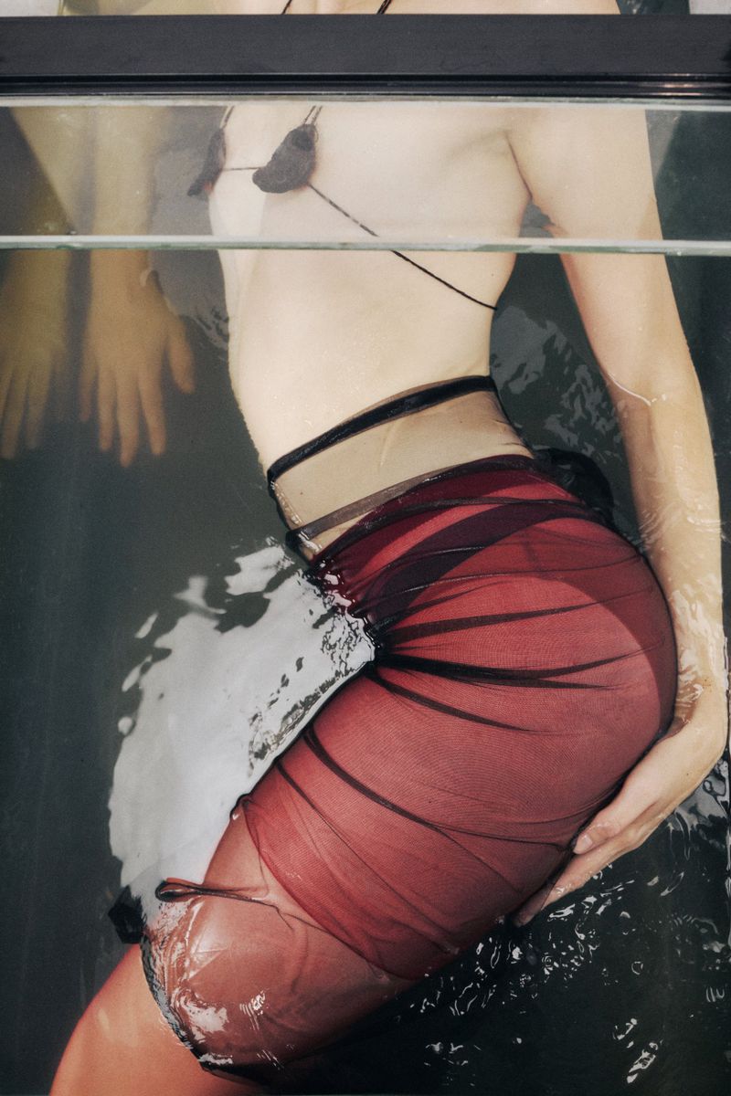 Woman in a black and red sheer dress partially submerged in water, captured in a close-up shot that focuses on the texture and colours of the fabric.