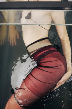 Woman in a black and red sheer dress partially submerged in water, captured in a close-up shot that focuses on the texture and colours of the fabric.