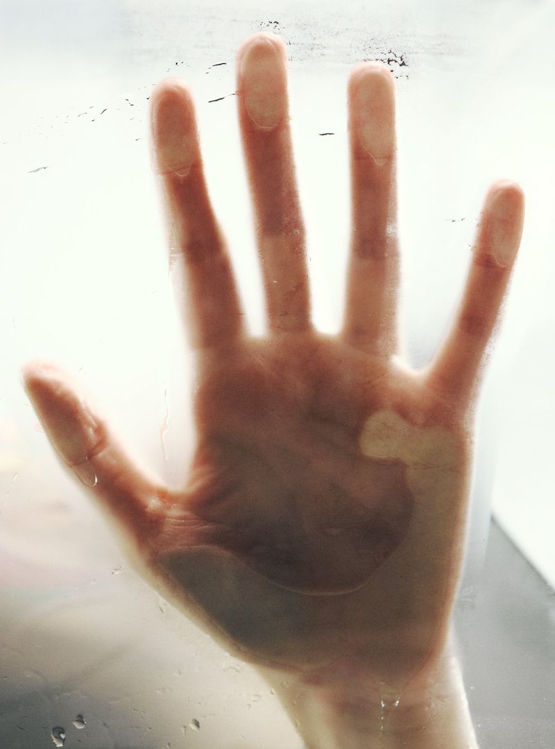 Close-up of a hand pressed against a glass surface with visible condensation and diffused lighting creates a sense of intimacy.