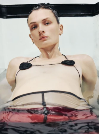 Woman in water wearing a black crocheted bikini top with heart-shaped cups and a translucent bottom, shot from a low angle.