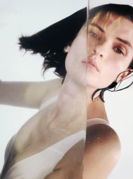 Model Lara Mullen partially visible through refracting water wearing a white swimsuit against a bright white studio backdrop.
